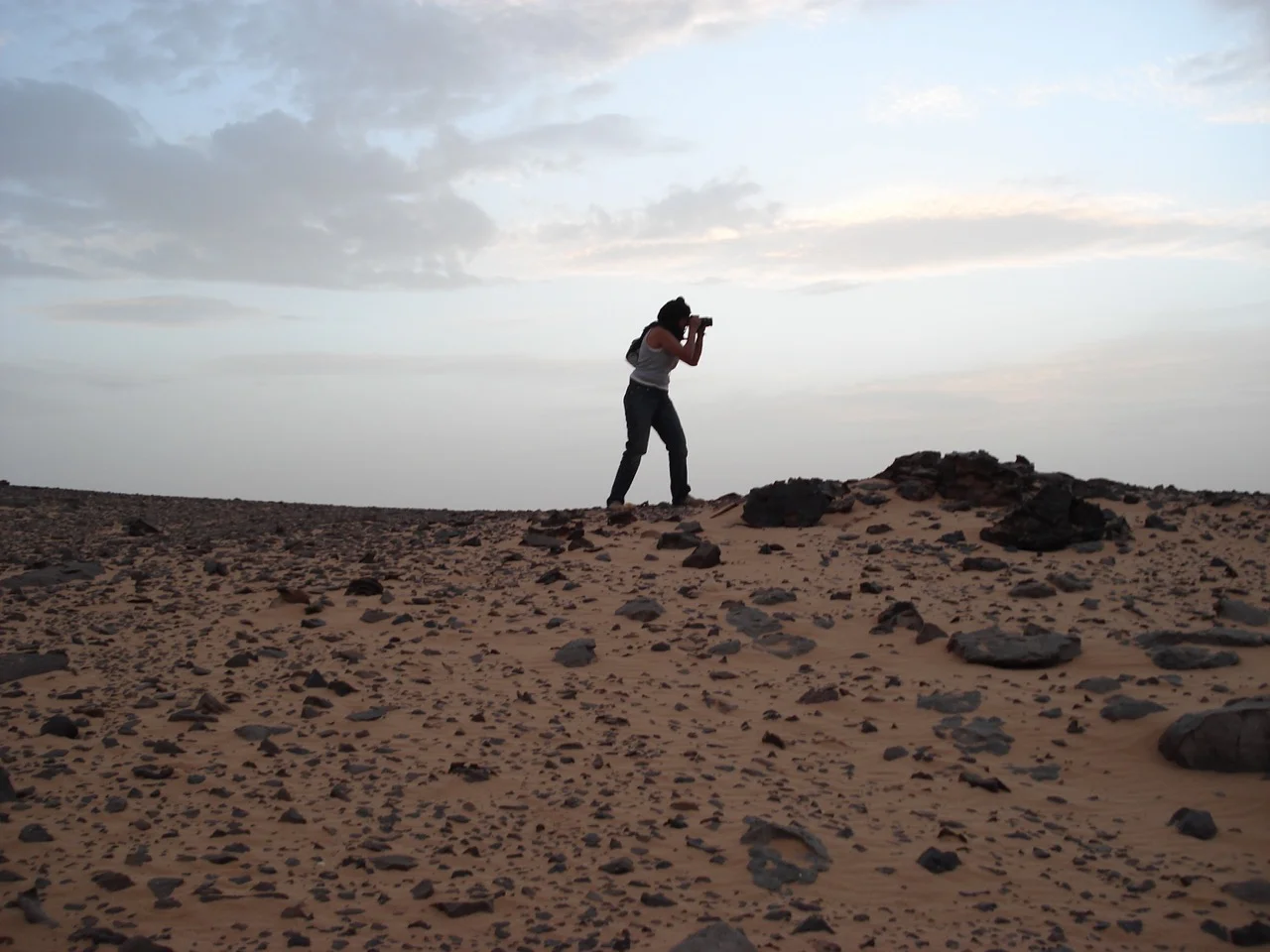 Farida Sellal photographiant, en silhouette au crépuscule dans le désert rocailleux